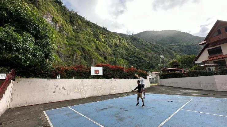Two people playing basketball on a court surrounded by green mountains