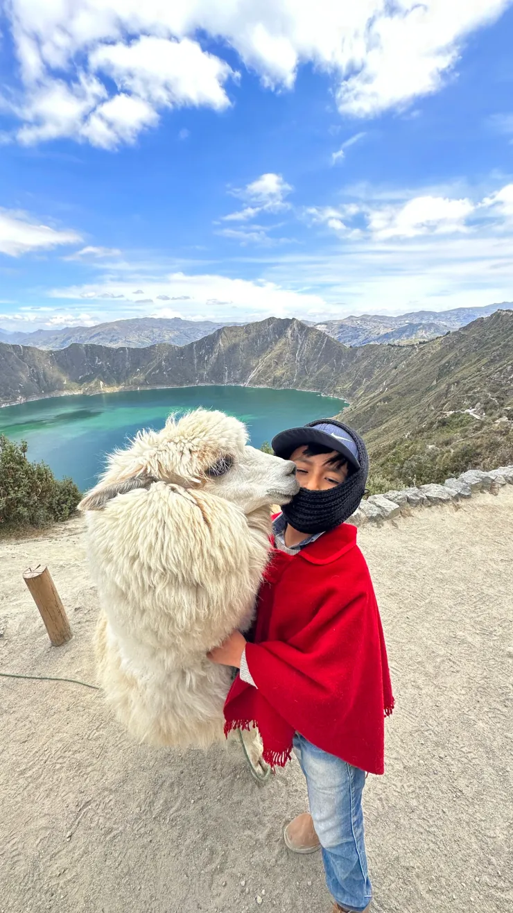A traveler embracing an alpaca beside a turquoise crater lake